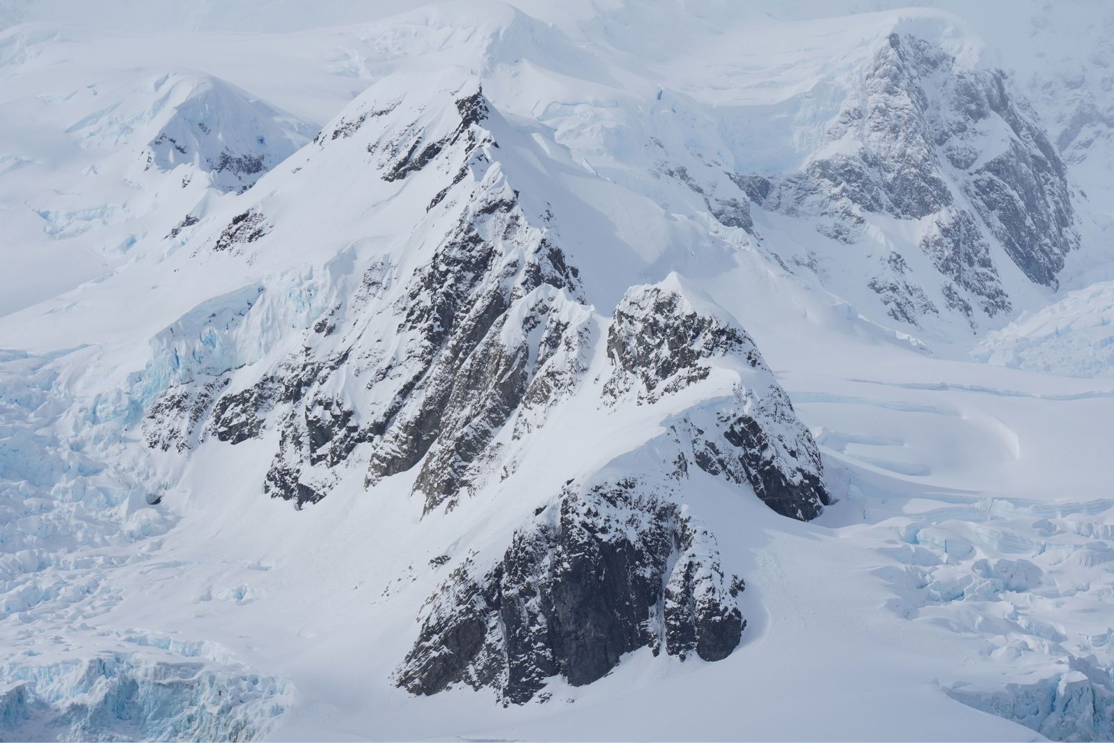 Snow-covered Antarctic mountain peaks with exposed dark rock and glaciers between steep ridges.