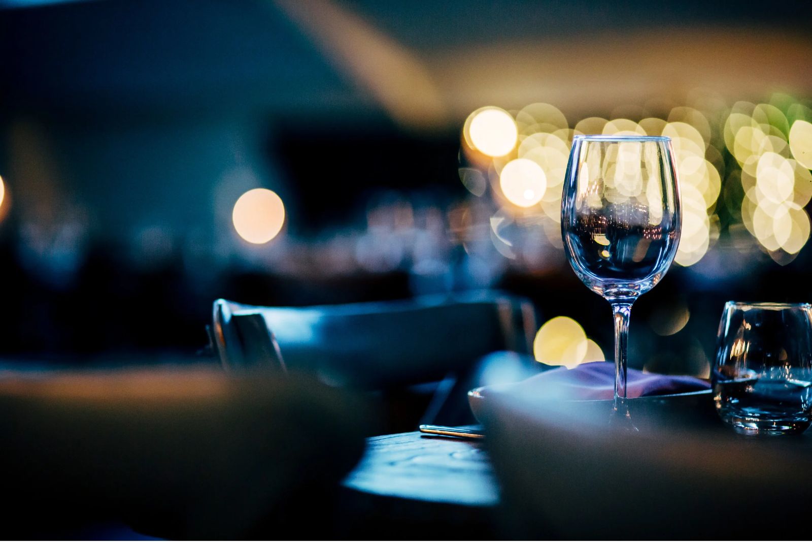 Wine glass and water glass on a restaurant table with softly glowing lights in the background.