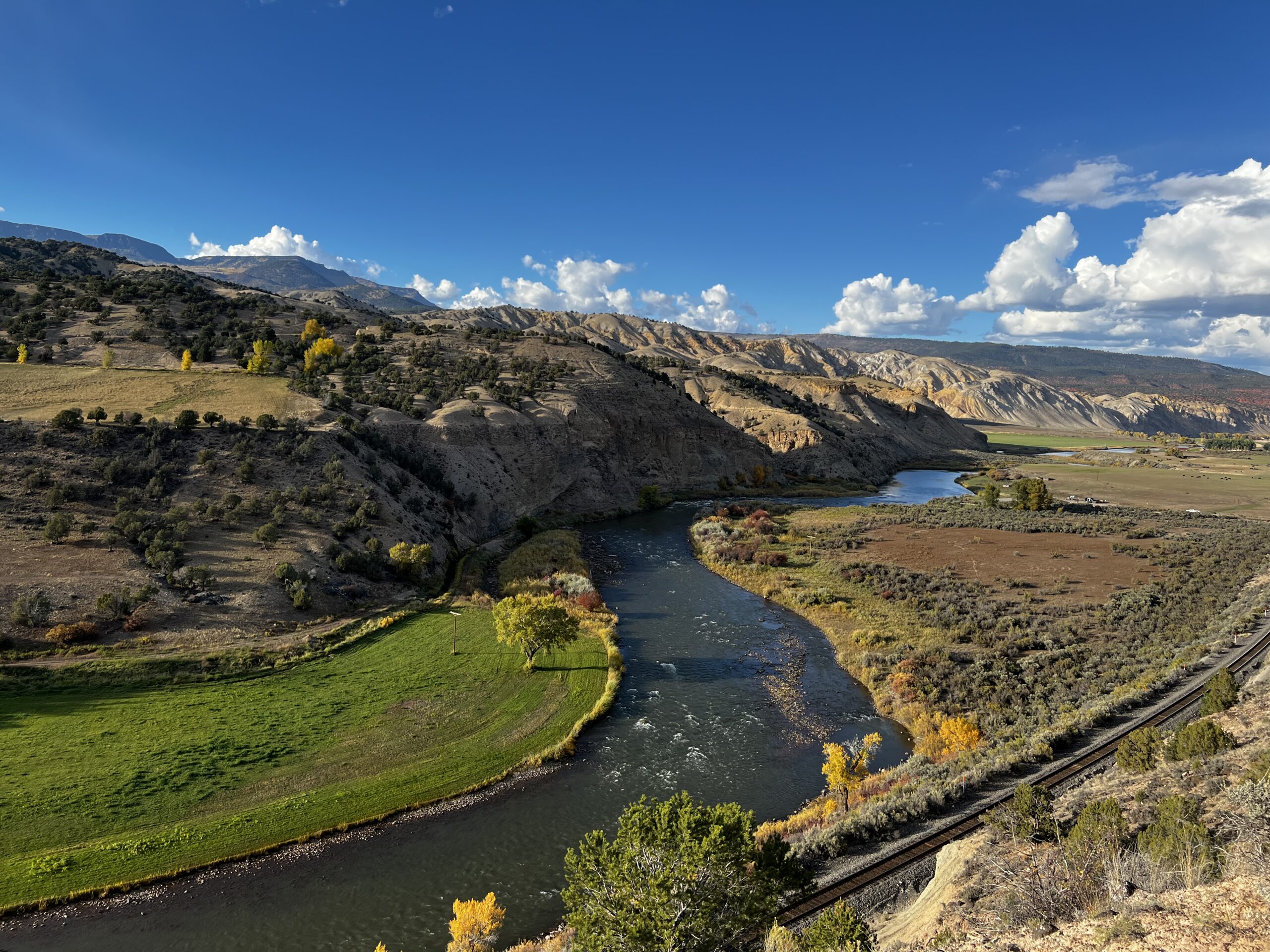 A river curves between green fields and rocky hills near Sweetwater, with autumn trees and railroad tracks along the bank.